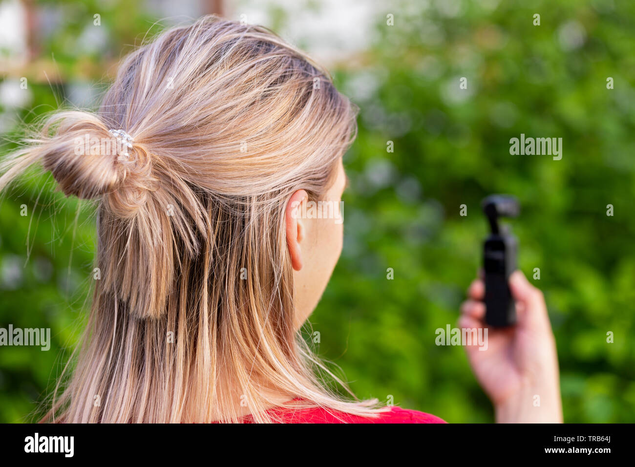 Junge blonde Frau mit osmo Kamera für vlogging Outdoor, grüner Hintergrund Stockfoto