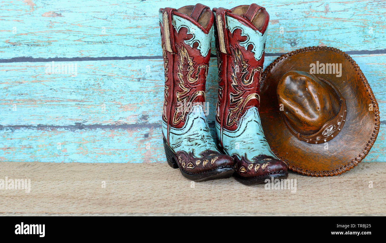 Ein Paar farbenfrohe, blaubraune Cowboy-Stiefel und Hut auf natürlichem Holz mit einem blaugrünigen Holzhintergrund Stockfoto