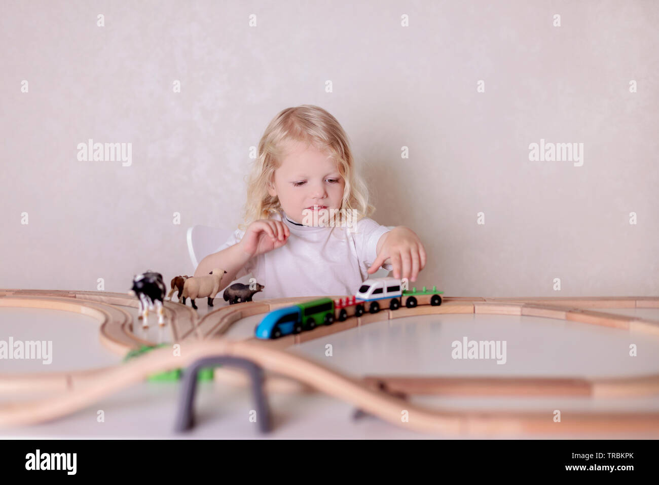 Kleinen Niedlichen baby boy (3 Jahre) trinkt Milch mit Cookies und spielt in den hölzernen Bahnhof in der Tabelle festgelegt. Selektive konzentrieren. Stockfoto