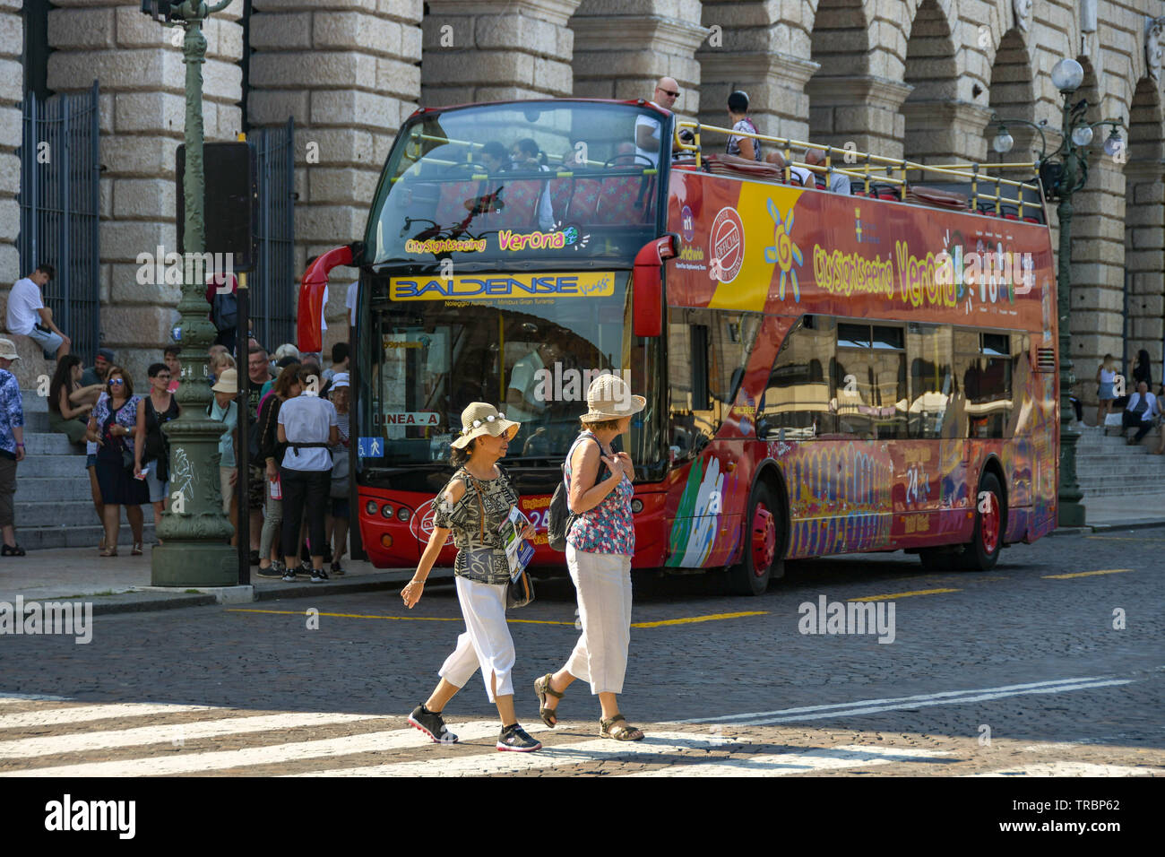 VERONA, ITALIEN - September 2018: Zwei Menschen überqueren die Straße auf einem Zebrastreifen in Verona. Im Hintergrund ist ein Hop-on Hop-off Bus Stockfoto