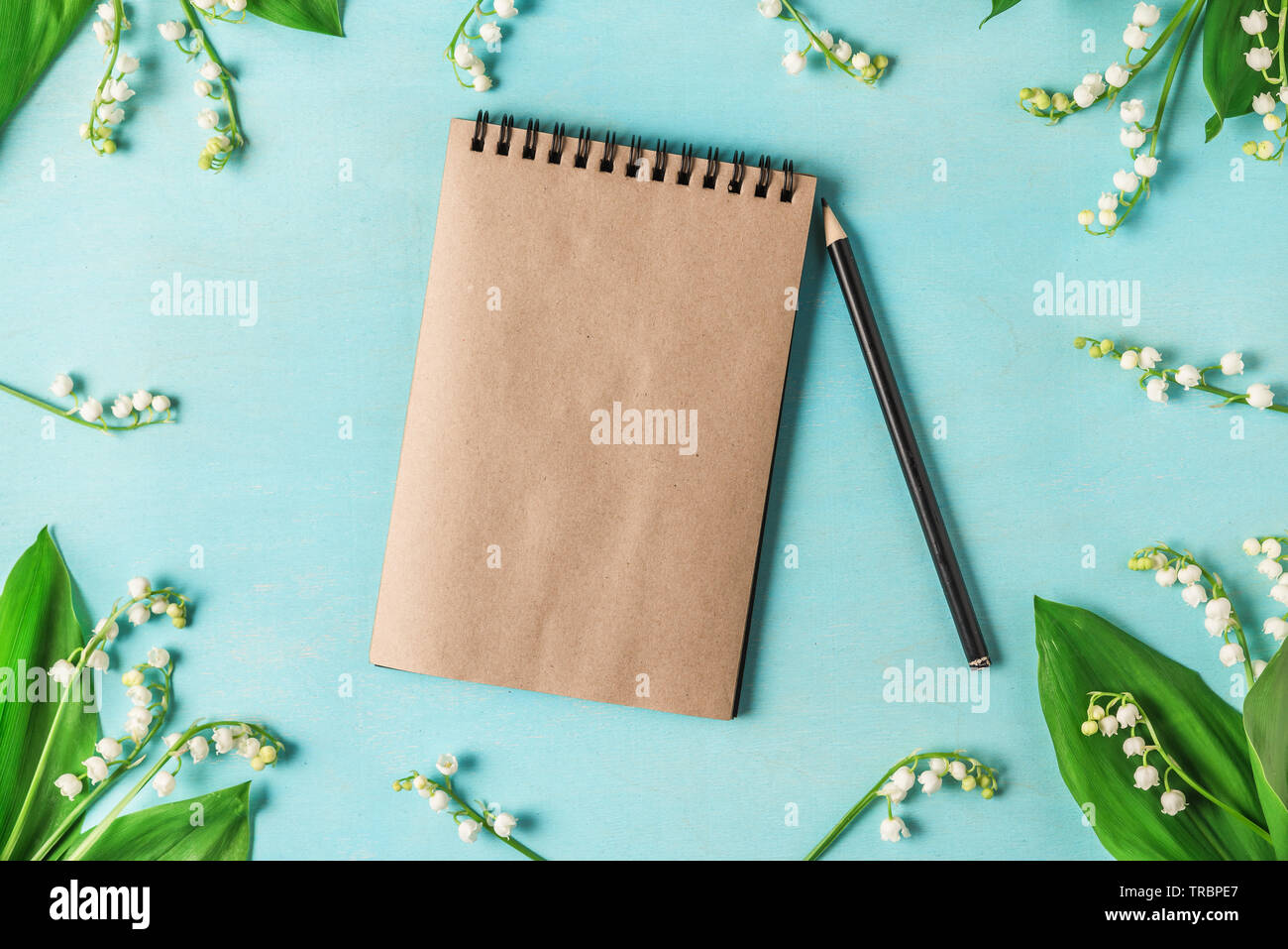 Leeres Papier Notebook im Rahmen von Maiglöckchen mit einem Bleistift auf Blau Holztisch. Flach. top anzeigen. Hochzeit Hintergrund Stockfoto