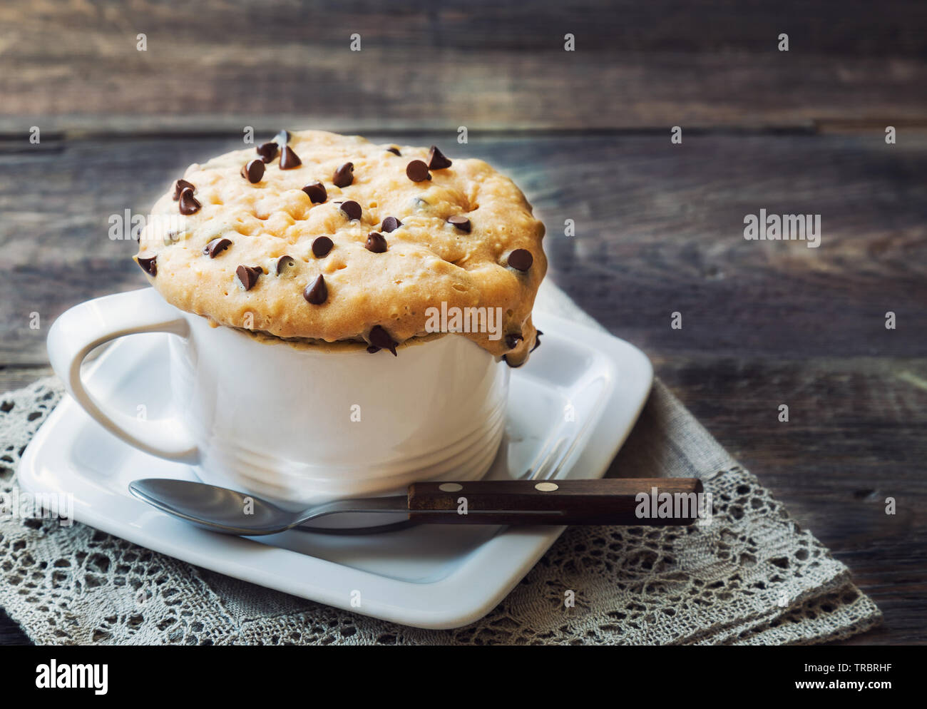 Frische hausgemachte Kuchen in Becher mit Erdnussbutter und Chocolate Chips auf rustikalen Holzmöbeln Hintergrund. In der Mikrowelle zubereitet. Stockfoto