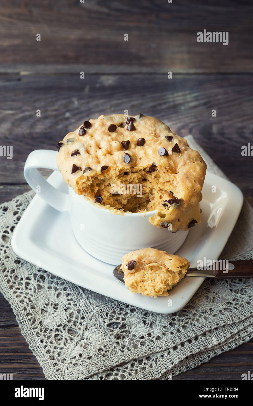 Frische hausgemachte Kuchen in Becher mit Erdnussbutter und Chocolate Chips auf rustikalen Holzmöbeln Hintergrund. In der Mikrowelle zubereitet. Stockfoto