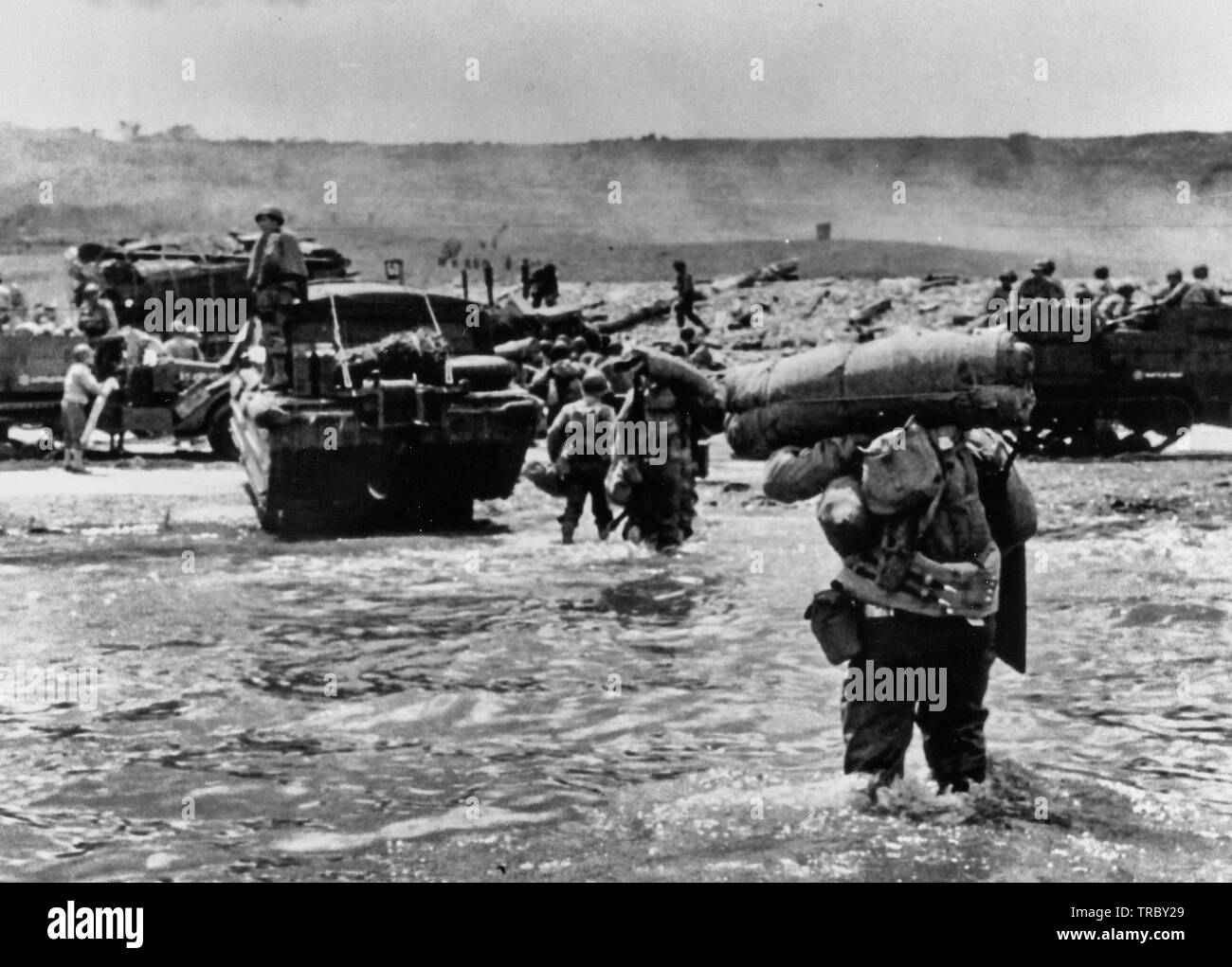 American assault Truppen mit voller Ausrüstung bewegen Sie auf Omaha Beach hinter schweren Material einschließlich der Hälfte - Titel und DUKWS. Rauch im Hintergrund ist von Naval geschützfeuer Unterstützung bei der Landung. Der Normandie. Juni 6, 1944. Stockfoto