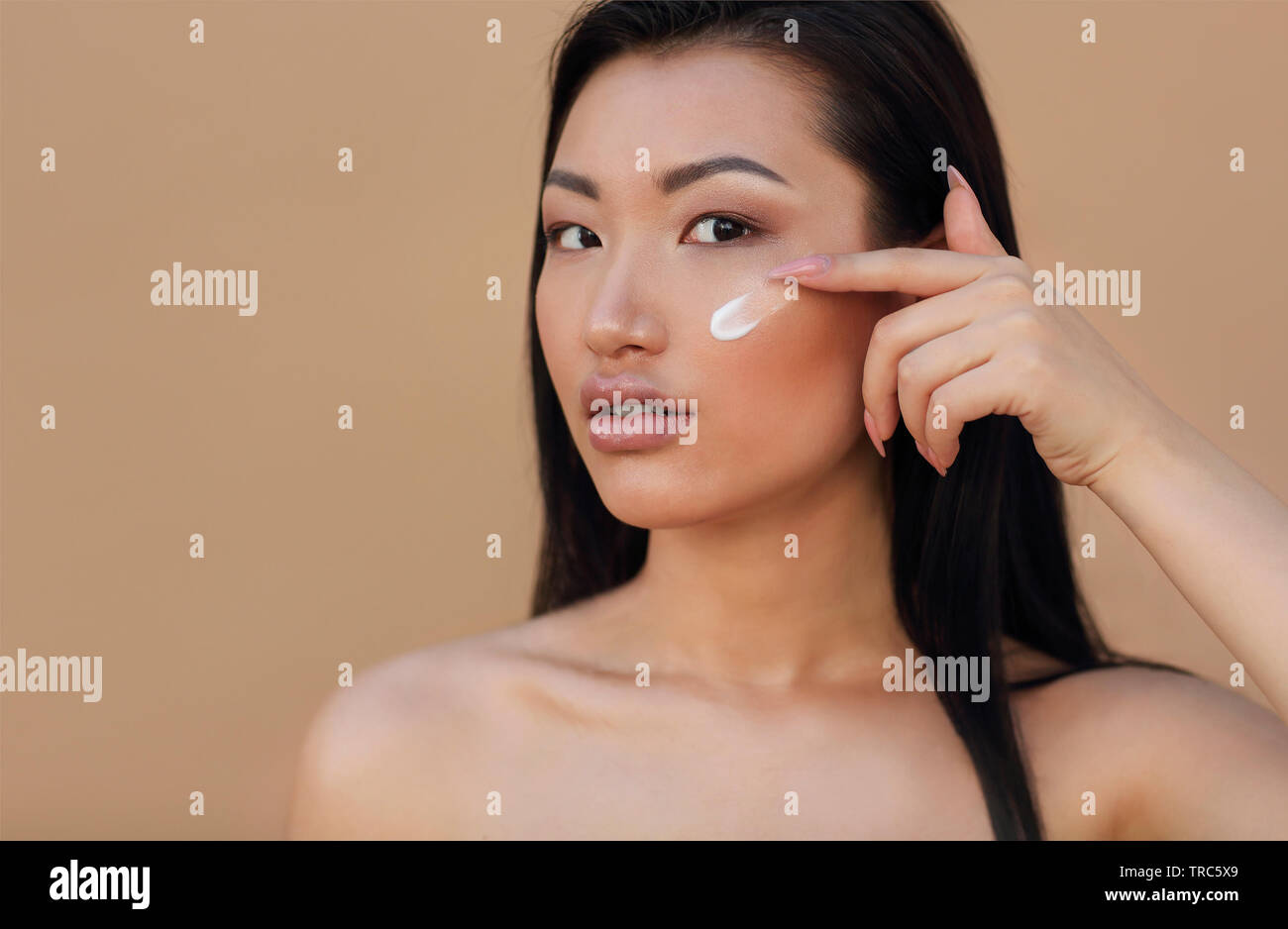 Junge schöne asiatische Frau Anwendung creme, beige Hintergrund isoliert Stockfoto
