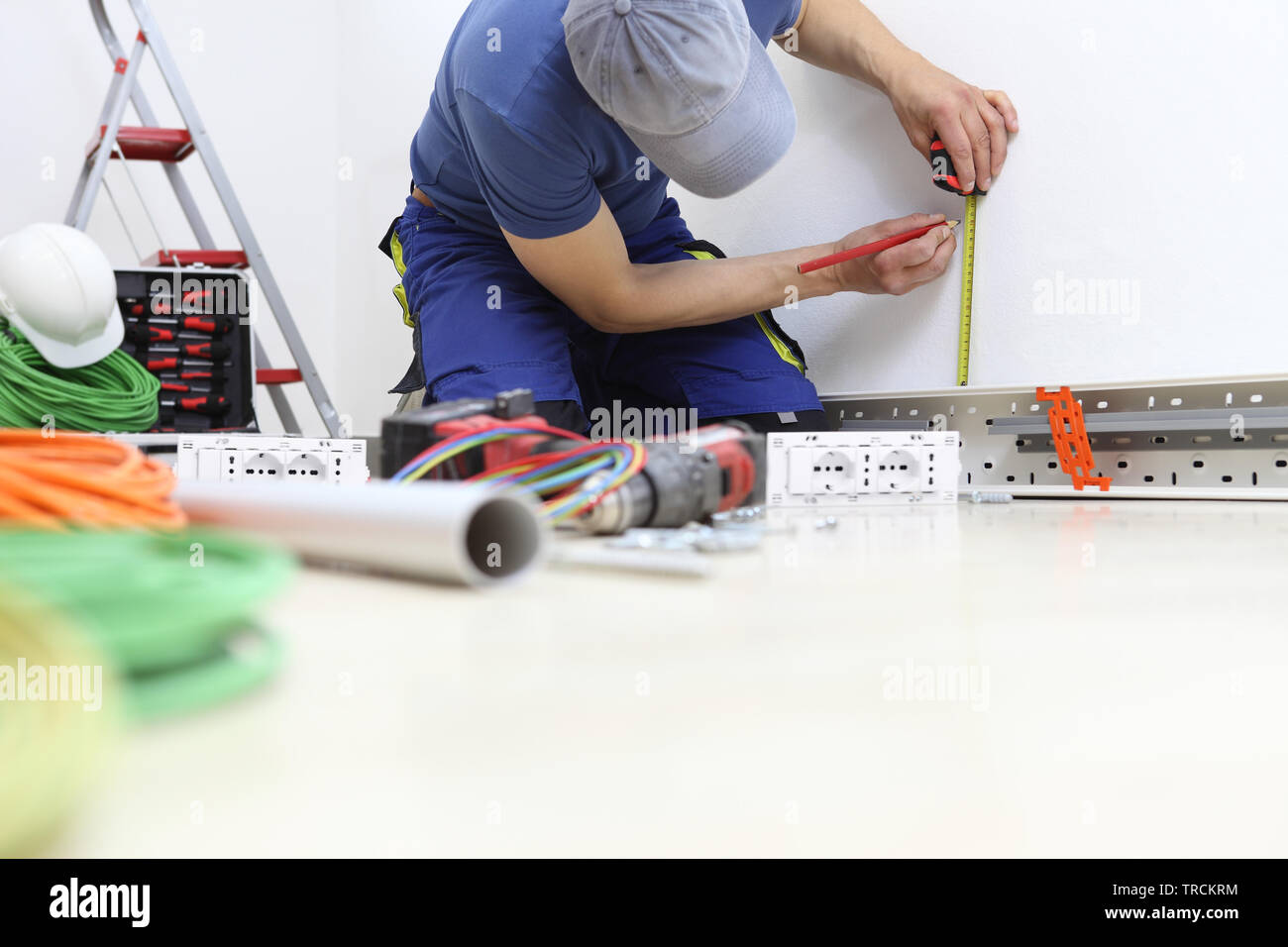 Elektriker bei der Arbeit mit Bleistift und Messgerät misst an der Wand die Position für die Steckdose, Stromkreise installieren, elektrische Verkabelung Stockfoto