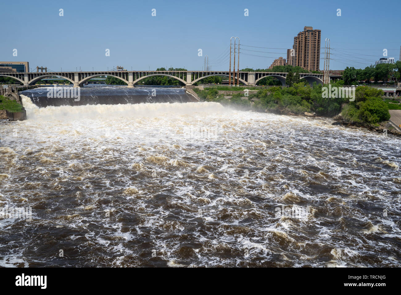 Weitwinkelaufnahme der St. Anthony Falls in der Innenstadt von Minneapolis, Central Avenue Bridge im Hintergrund. Schnelle Strömungen erstellen schaumigen Wasser Stockfoto