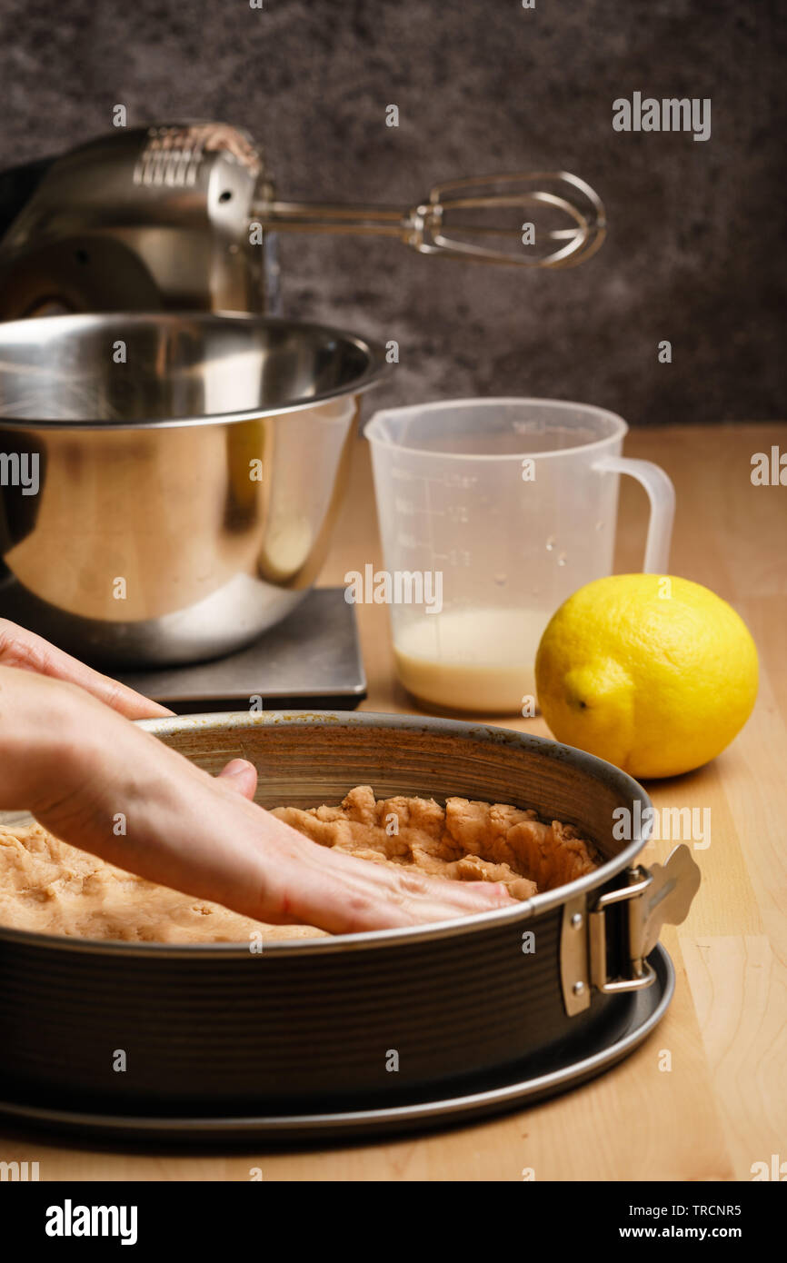 Zwei weiblichen kaukasischen Hände aus den rohen Teig verteilt in einem schwarzen Backblech, backen Geschirr in den Hintergrund - Seitenansicht, Hochformat Stockfoto