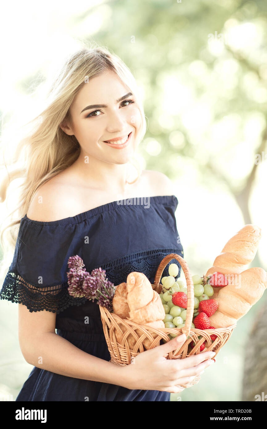 Lächelnde blonde Mädchen 22-24 Jahre alten Holding Korb mit Essen im Freien. Mit Blick auf die Kamera. 20. Stockfoto