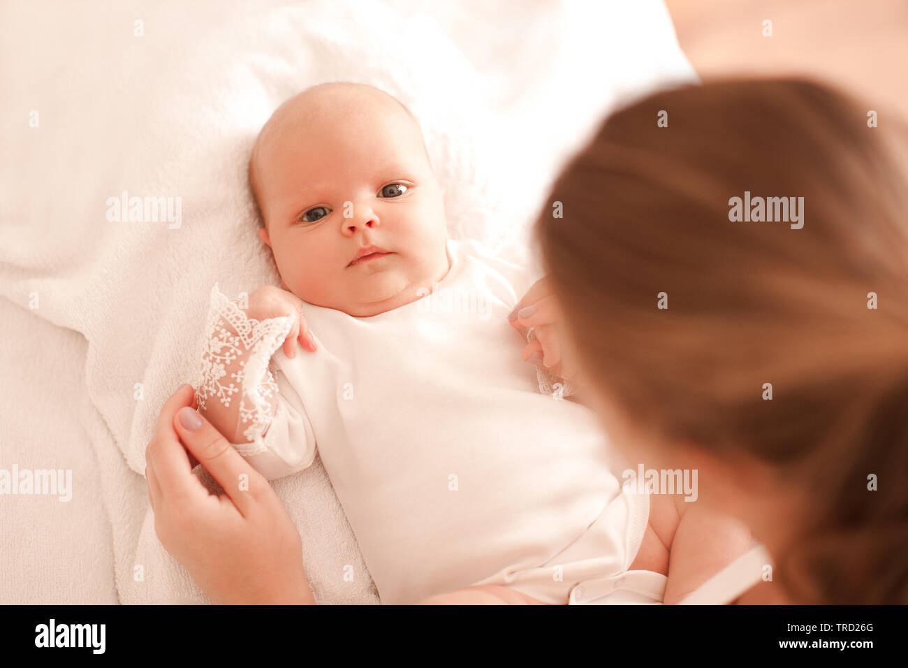 Mutter Holding baby girl im Bett zuhause liegen. Mit Blick auf die Kamera. Die Mutterschaft. Mutterschaft. Ansicht von oben. Stockfoto