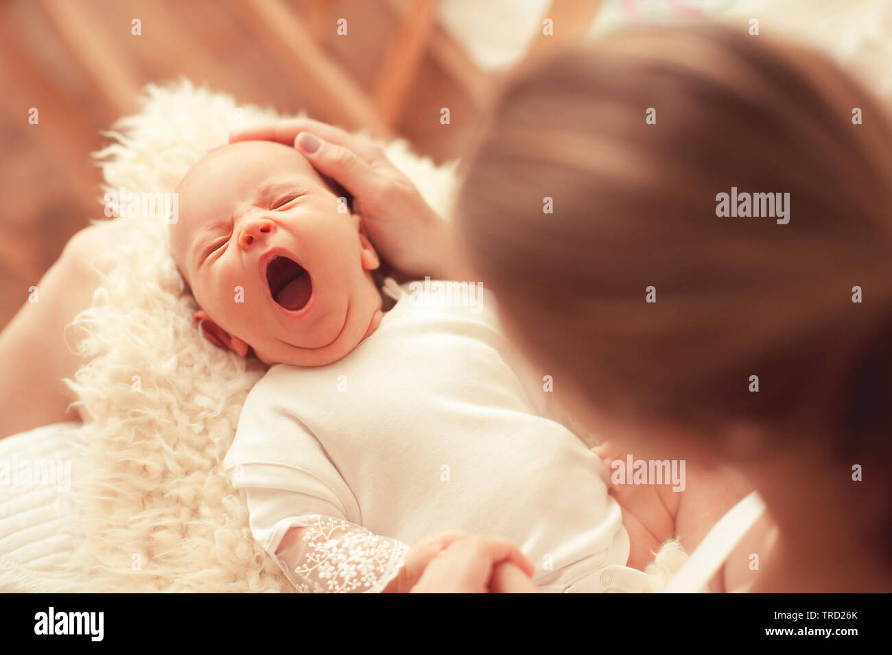 Cute gähnen Kleinkind Baby auf Mütter Hände im Zimmer. Die Mutterschaft. Mutterschaft. Kindheit. Stockfoto