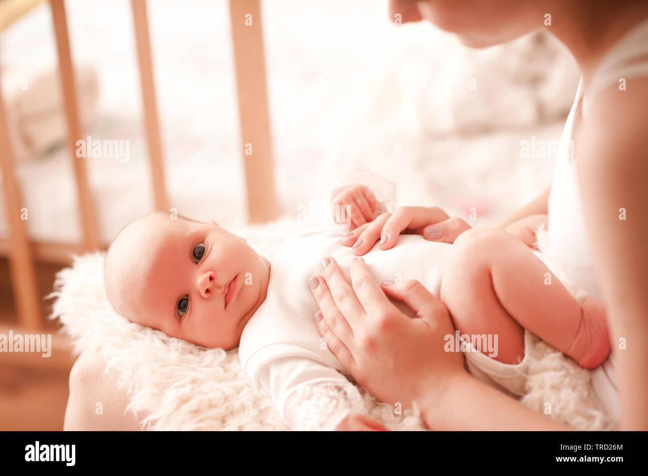 Cute Baby Mädchen liegt auf Mütter Hände im Innenbereich. Mutter berühren Kleinkind im Zimmer. Mit Blick auf die Kamera. Die Mutterschaft. Mutterschaft. Stockfoto