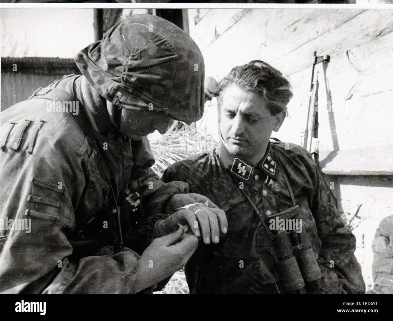 5. SS Panzer Division Sturmbannführer großer Hack in Camouflage Smock erhält erste Hilfe für leichte Wunde von einem Arzt an der Ostfront vor 1944 im Hintergrund seine MP 44 Stockfoto