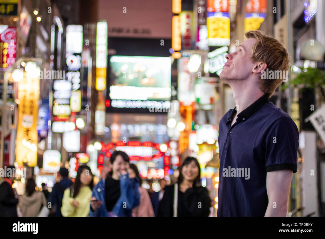 Einen gutaussehenden blonden Touristen auf der Suche von der Seite auf einem neon Tokyo street Stockfoto
