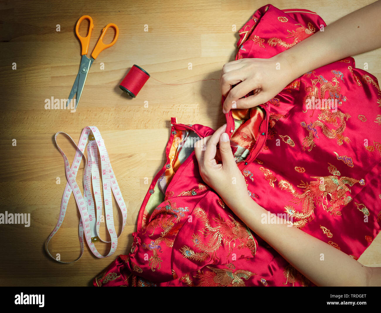 Blick von oben auf die 7/8-weibliche Hände nähen Cheongsam Kleid mit Nadel im Näherin Arbeitsplatz mit Näheinrichtungen Stockfoto