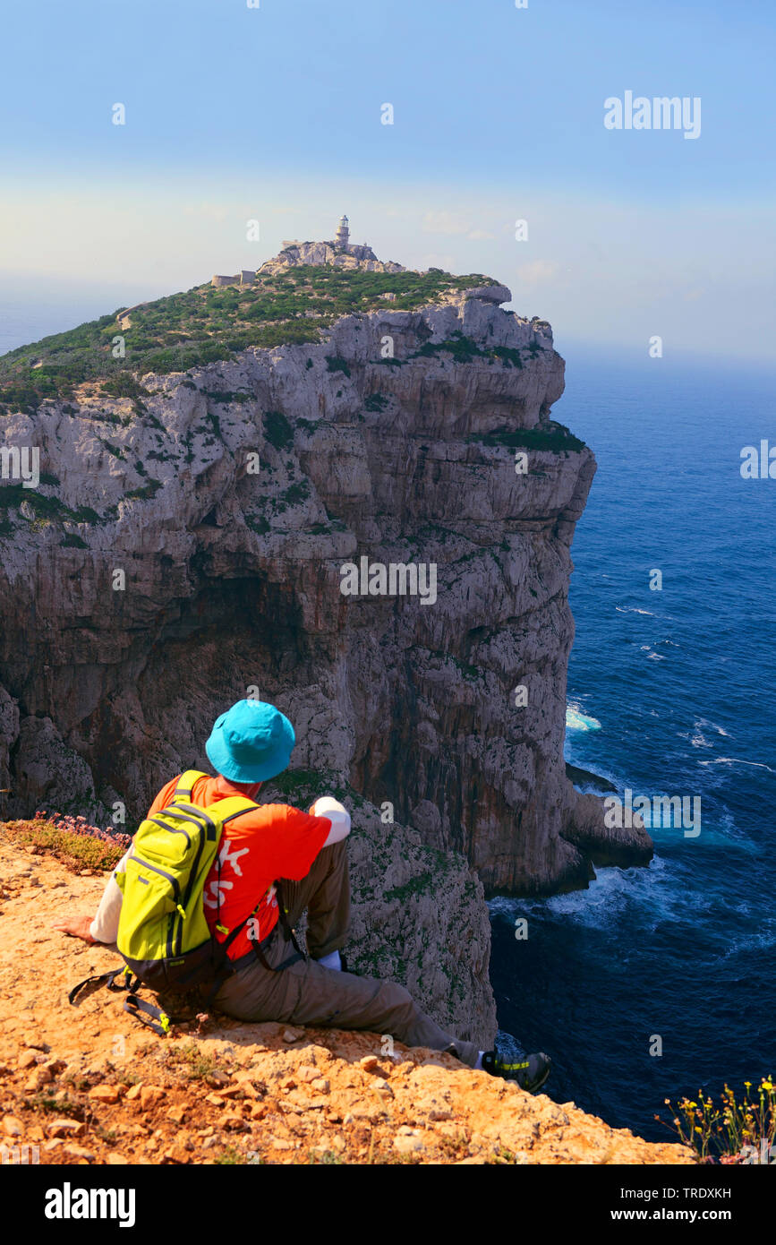 Wanderer sitzen am Rande eines speep Gesicht und am Leuchtturm von Capo Caccia, Italien, Sardinien, Alghero suchen Stockfoto
