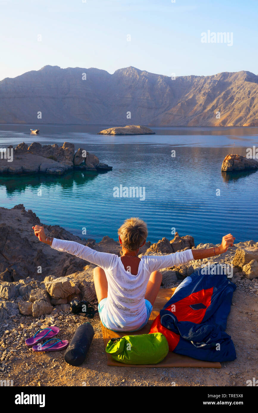 Frau erwachen nach outdoor Übernachtungen an der felsigen Küste der Straße von Hormuz, Oman, Shamamar, Khasab Stockfoto