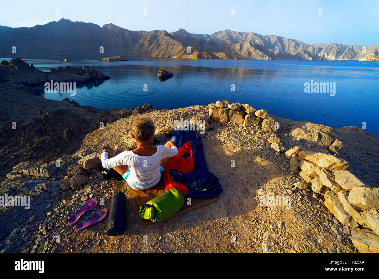 Frau erwachen nach outdoor Übernachtungen an der felsigen Küste der Straße von Hormuz, Oman, Shamamar, Khasab Stockfoto