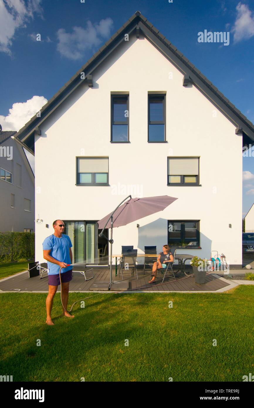 Paare, die in der Garten von einem neu gebauten Einfamilienhaus, Mann, den Garten zu bewässern Stockfoto