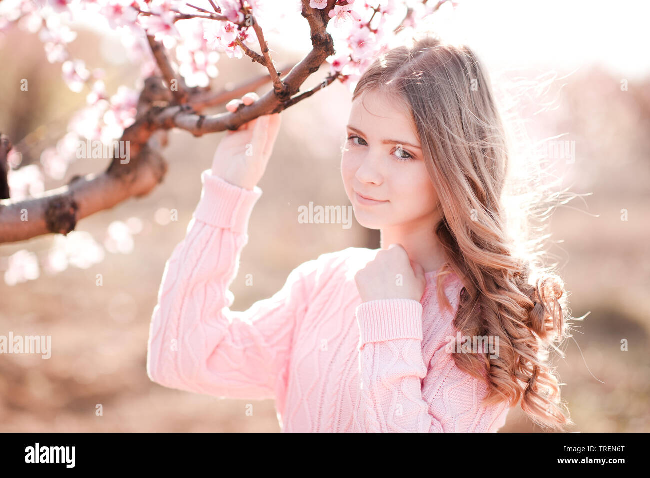 Schönes blondes junges Mädchen 14-16 Jahre alten Holding pfirsich Baum im Garten. Posing im Freien. Gestrickte Pullover tragen. Weg schauen. Stockfoto