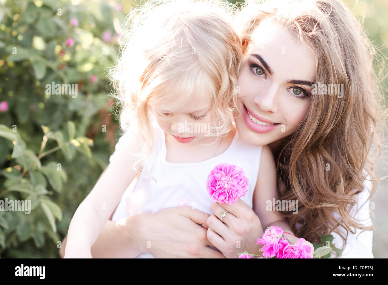Lächelnde Mutter Holding Baby Mädchen 3-4 Jahre alten mit Blumen im Freien. Mit Blick auf die Kamera. Die Mutterschaft. Sommer Saison. Stockfoto