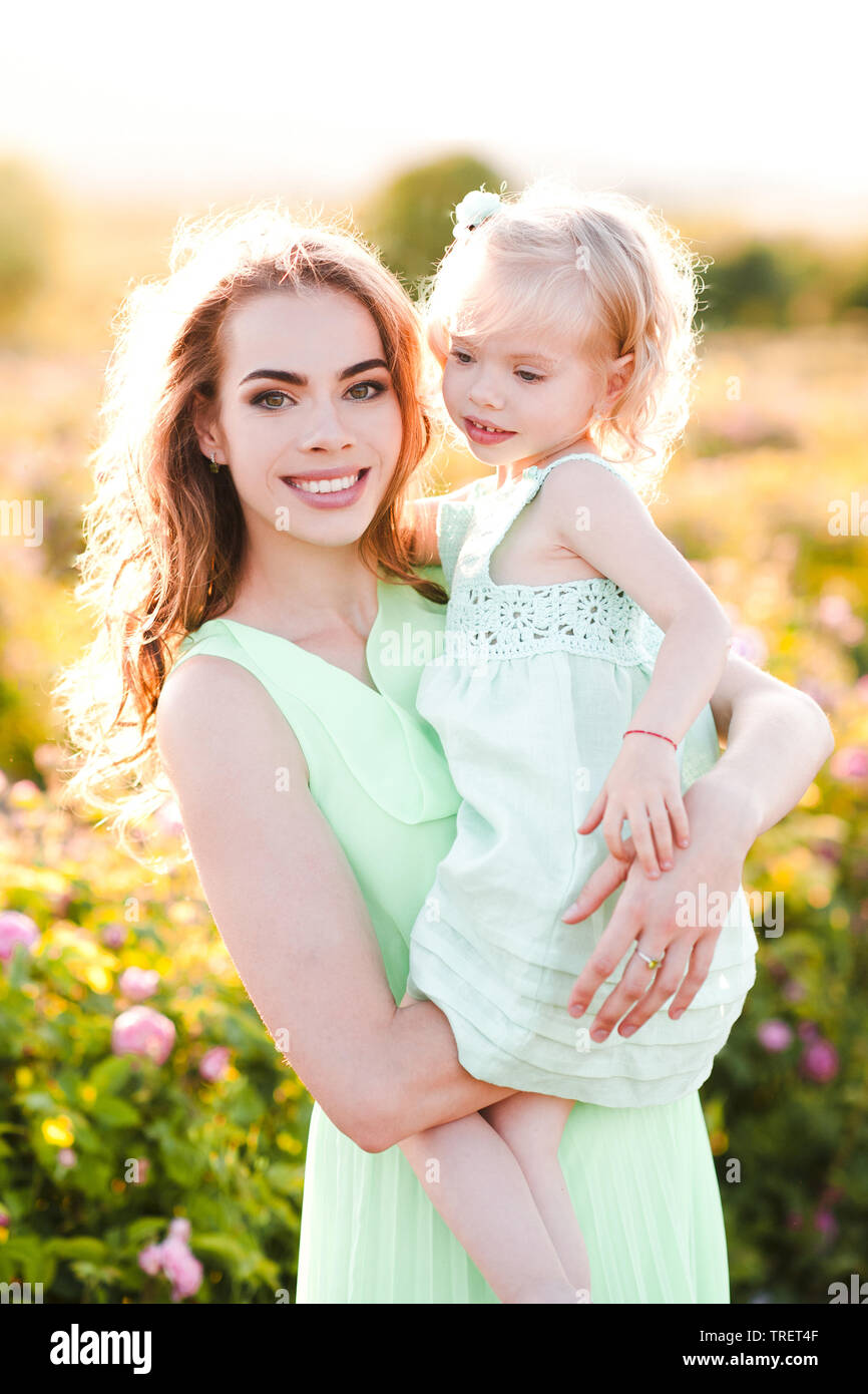 Lächelnde Frau mit Baby Mädchen 3-4 Jahre alten über sonnige Natur Hintergrund. Mit Blick auf die Kamera. Die Mutterschaft. Stockfoto