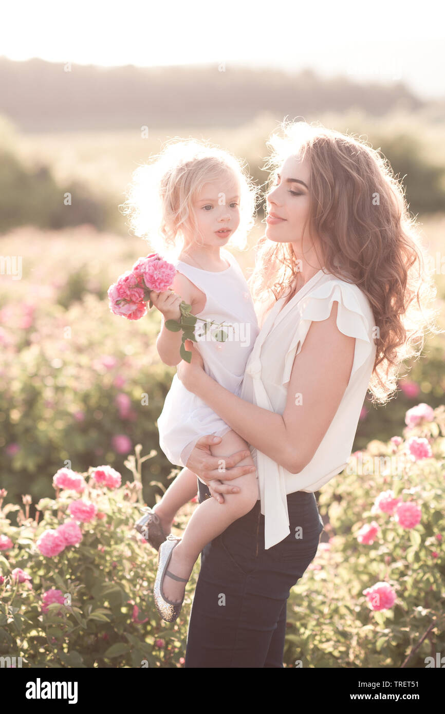 Lächelnde Mutter ihr Kind Tochter Holding in Rose Feld. Legere Kleidung im Freien. Zeit mit der Familie. Stockfoto