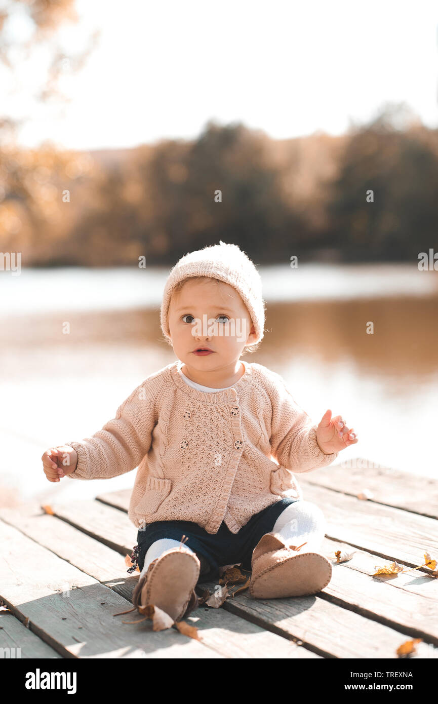 Cute Baby girl 1 Jahr alt tragen stilvolle aus Gewirken Kleider im Herbst Park im Freien posieren. Mit Blick auf die Kamera. Stockfoto