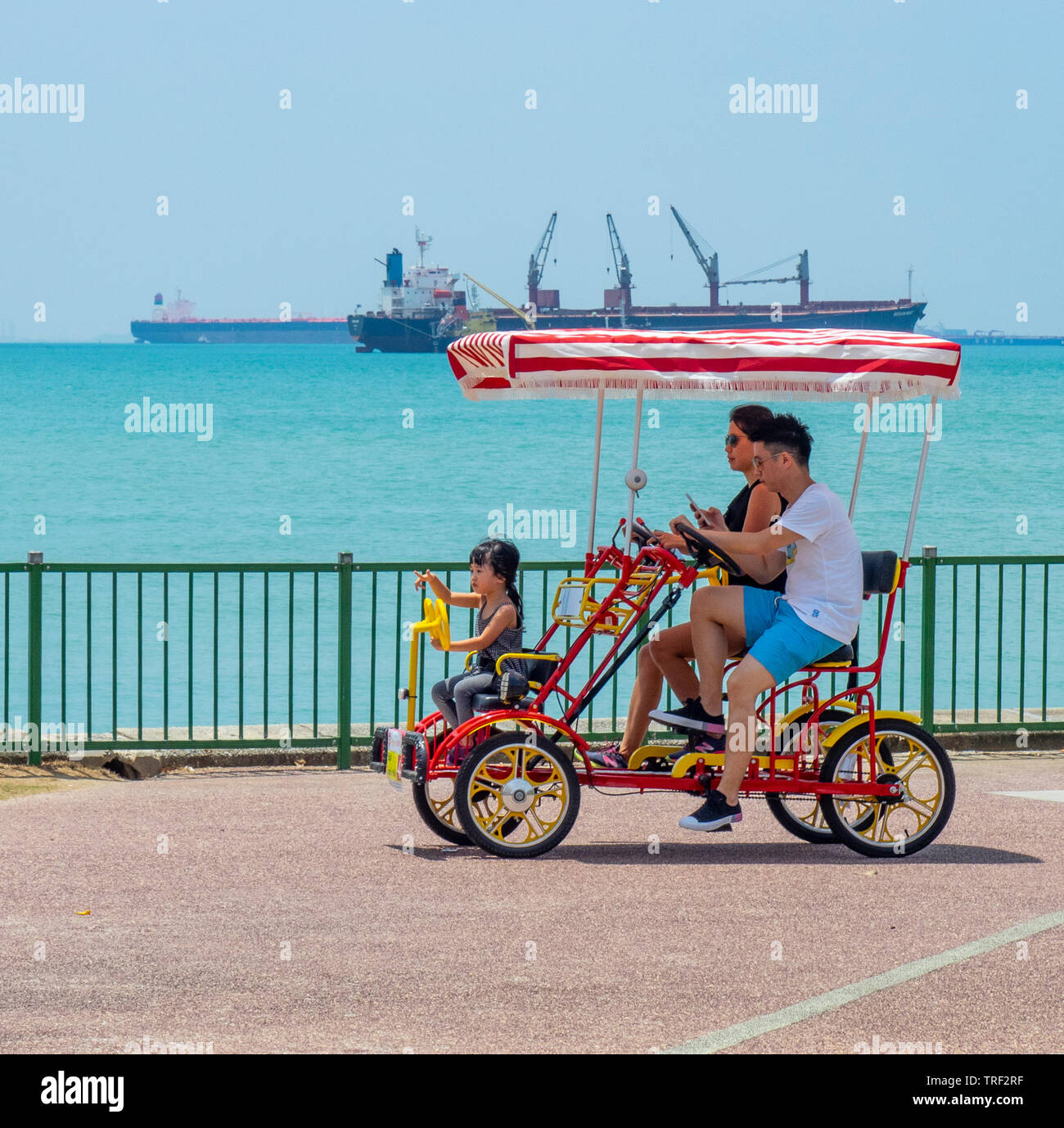 Familie Reiter einen Mietwagen quadracycle an der East Coast Park, Frachtschiffe im Hintergrund Singapur. Stockfoto