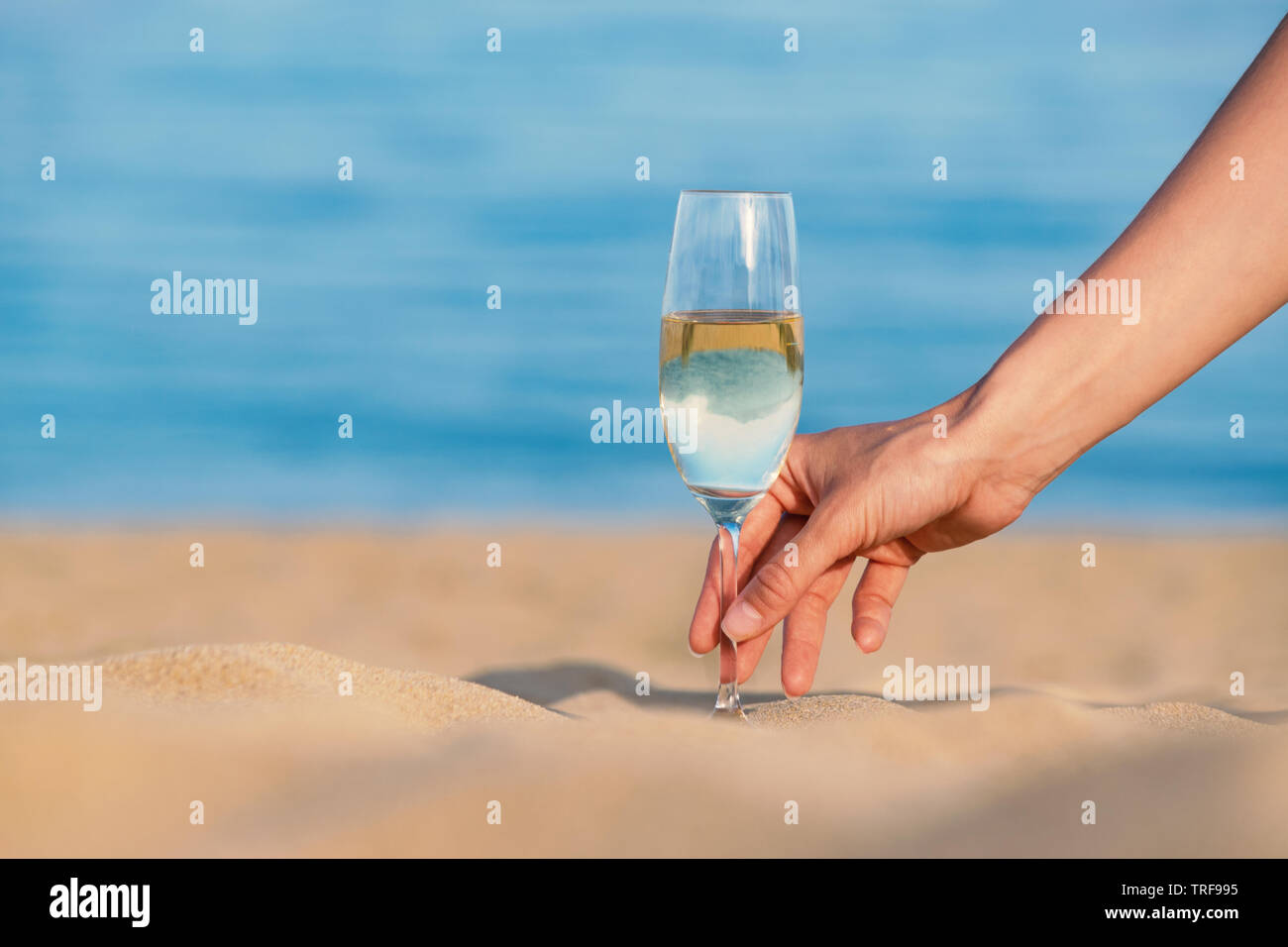 Weibliche hand Glas Champagner gegen blaue Meer. Selektiver Fokus, unscharfen Hintergrund, Platz für Text Stockfoto