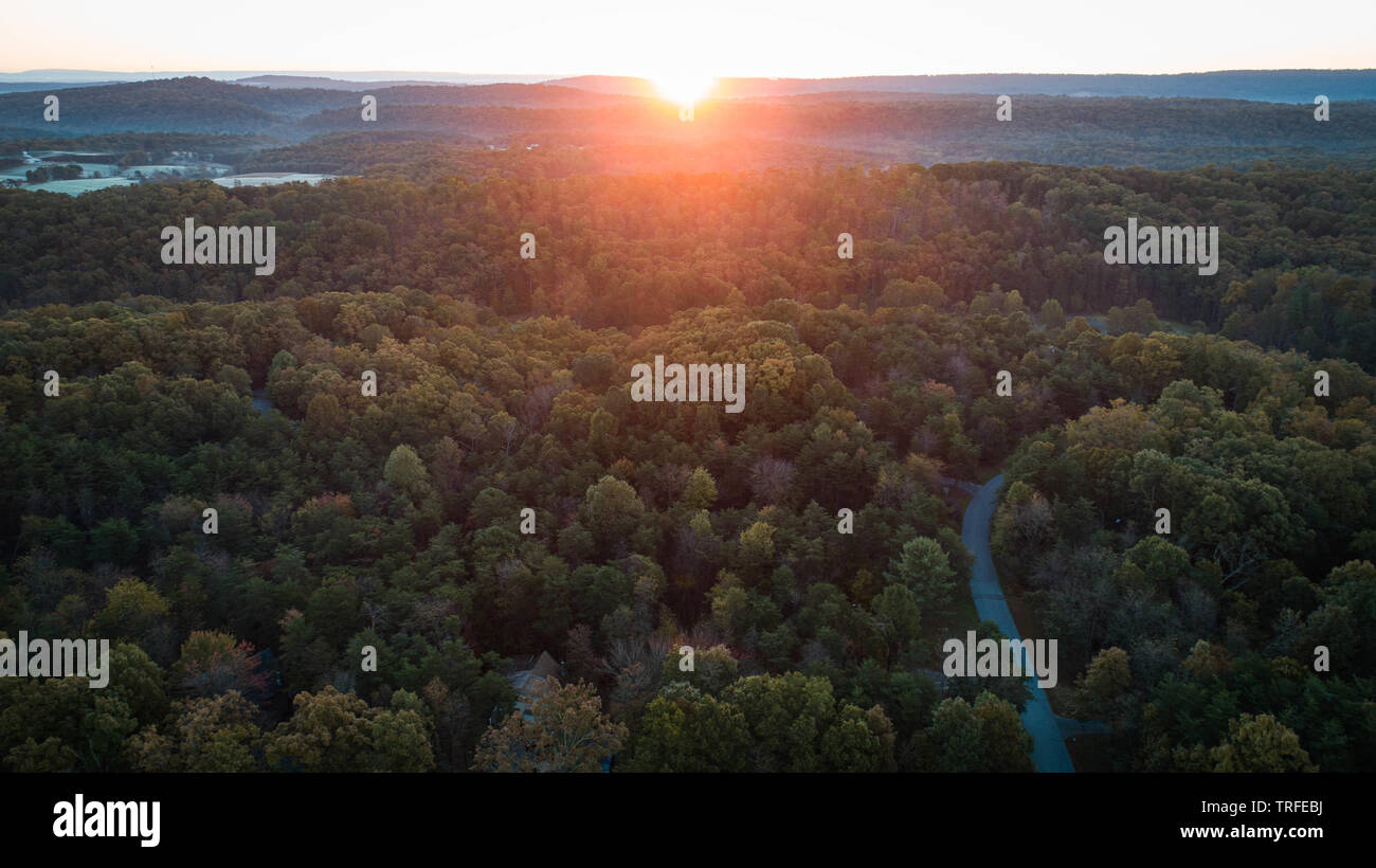 Malerische Sonnenaufgang am frühen Morgen Ansicht luftbild Drohne Foto Suchen auf Tree Tops kurvenreiche Straße schönen Sonnenaufgang über den Bergen Hügel im Horizont Stockfoto