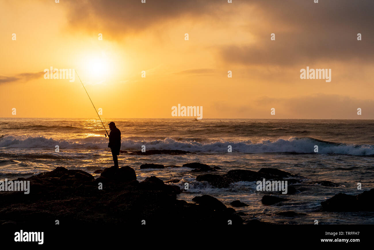 Lone Fischer auf dem Felsen während der schönen Sonnenaufgang am Strand. Durban, East Coast, Südafrika Stockfoto