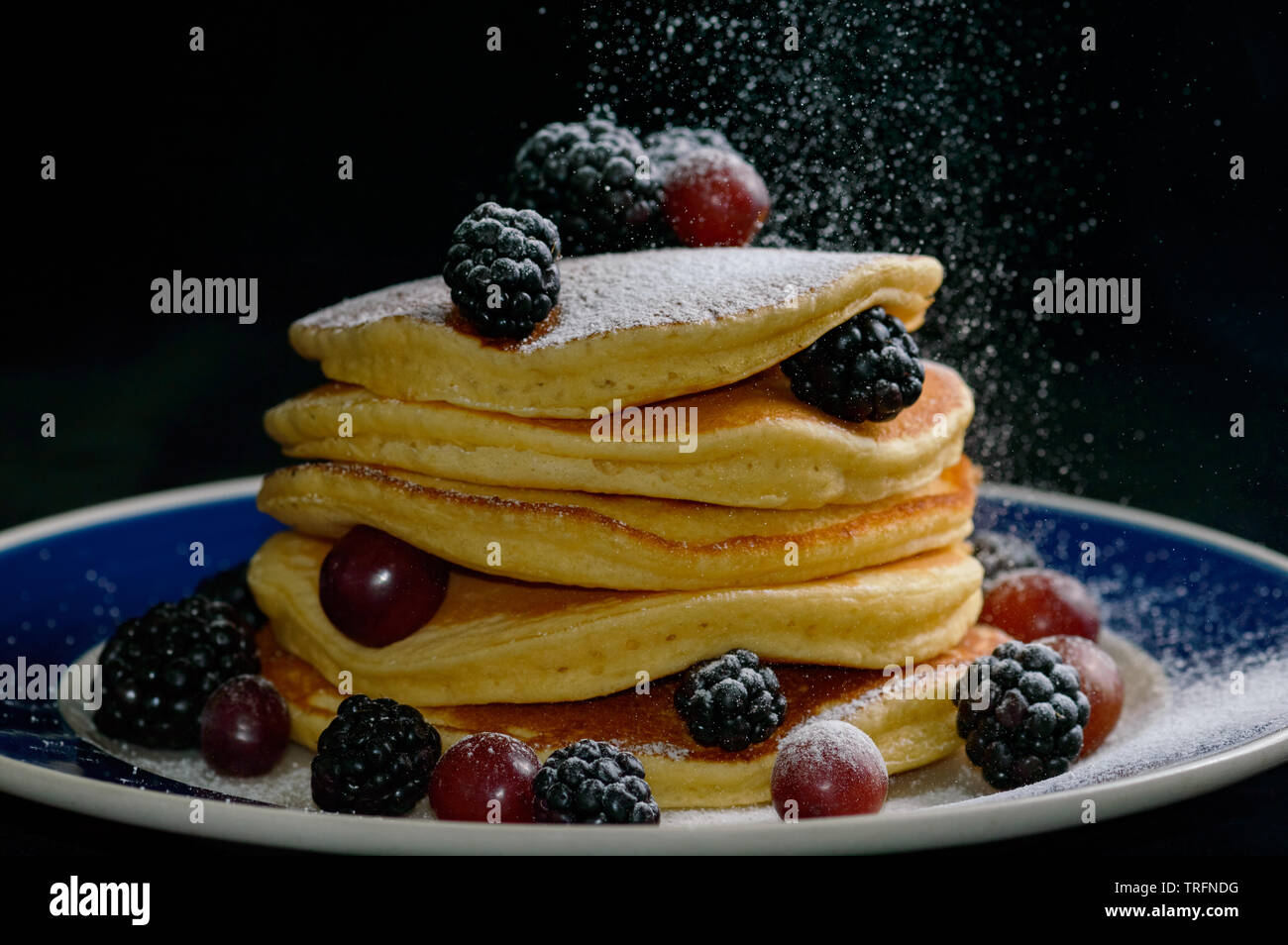 Gestapelte Pfannkuchen mit Sommer Beeren und fallende Konditoren Zucker, isoliert auf Schwarz. Stockfoto