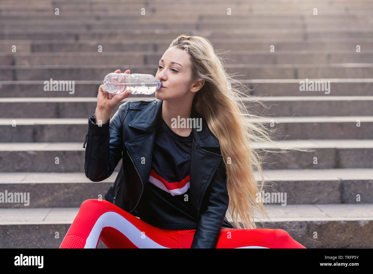 Junge Frau in Active Wear sitzen auf Treppen mit Wasserflasche. sie trägt rote Übung Hosen und rote Schuhe. Stockfoto