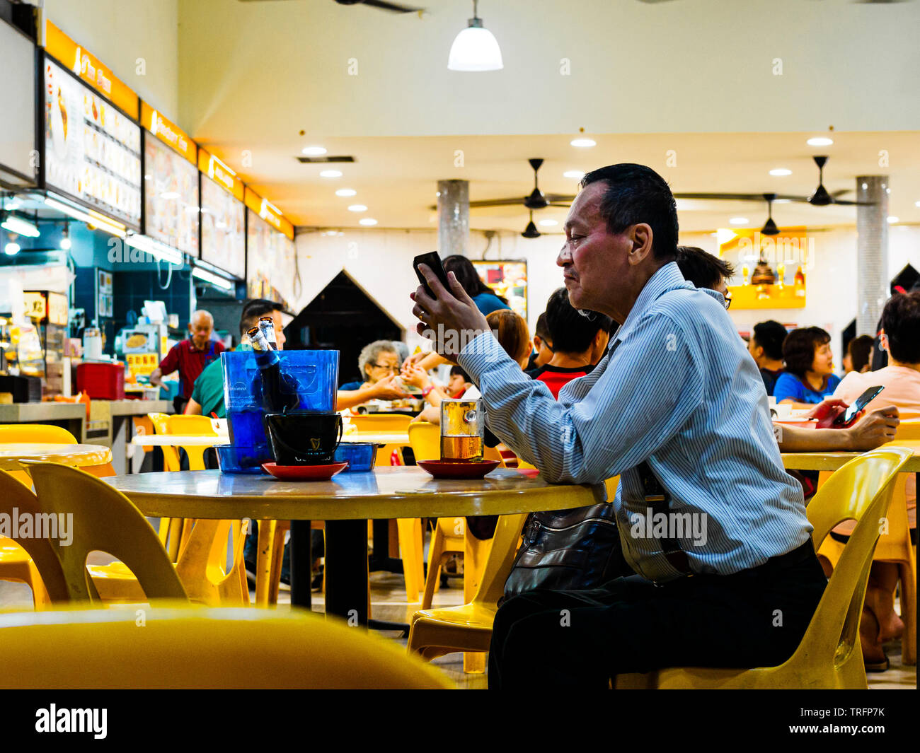 Singapur - 17 Mär 2019 - ein Mann mittleren Alters in der Bürokleidung bis spät in die Nacht Bier genießt in einem Restaurant/Cafe/das kopitiam, / Hawker Center Stockfoto