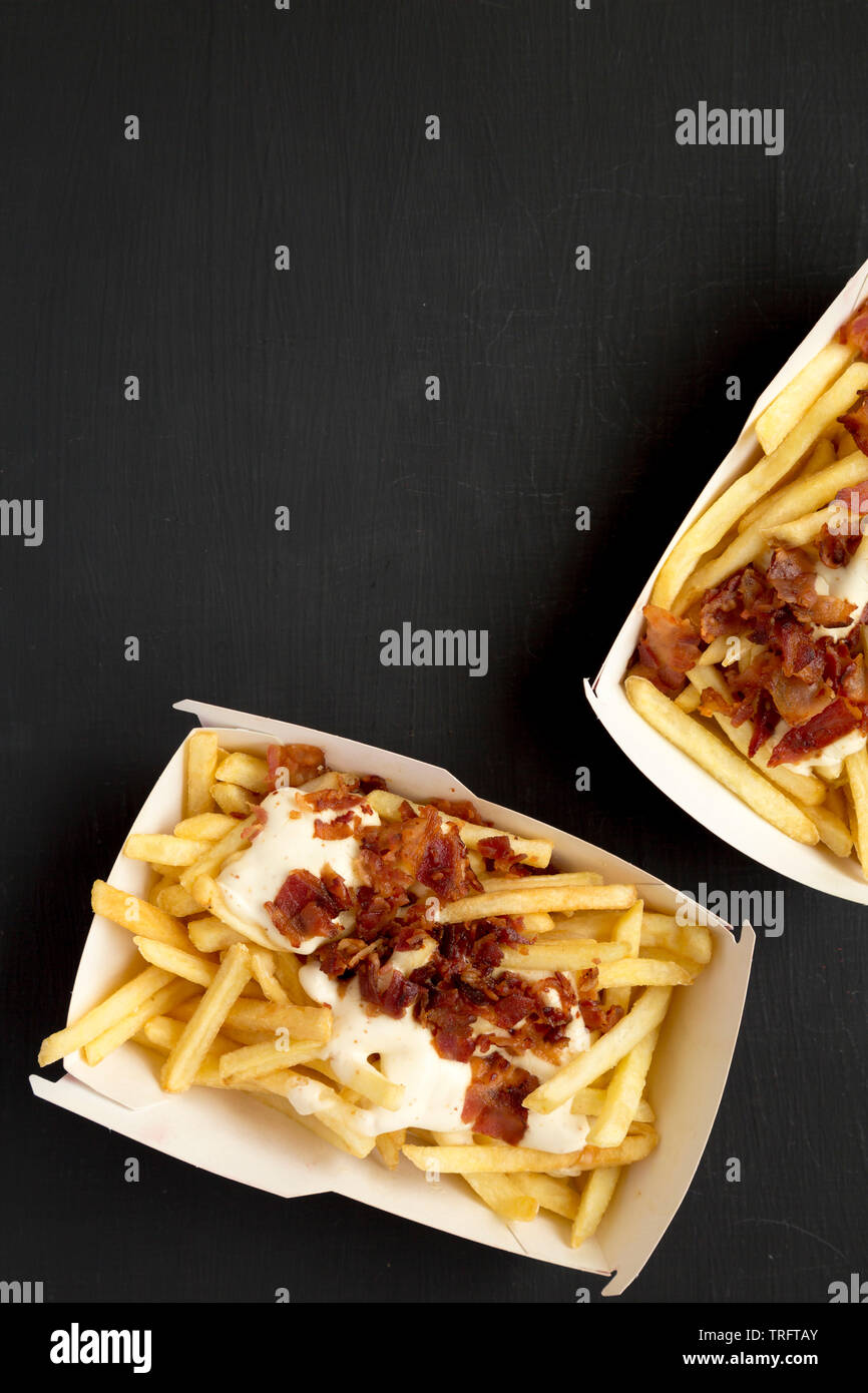 Pommes Frites mit Käsesoße und Speck in Papier Boxen über schwarzen Oberfläche. Flach, von oben, Overhead, Ansicht von oben. Kopieren Sie Platz. Stockfoto