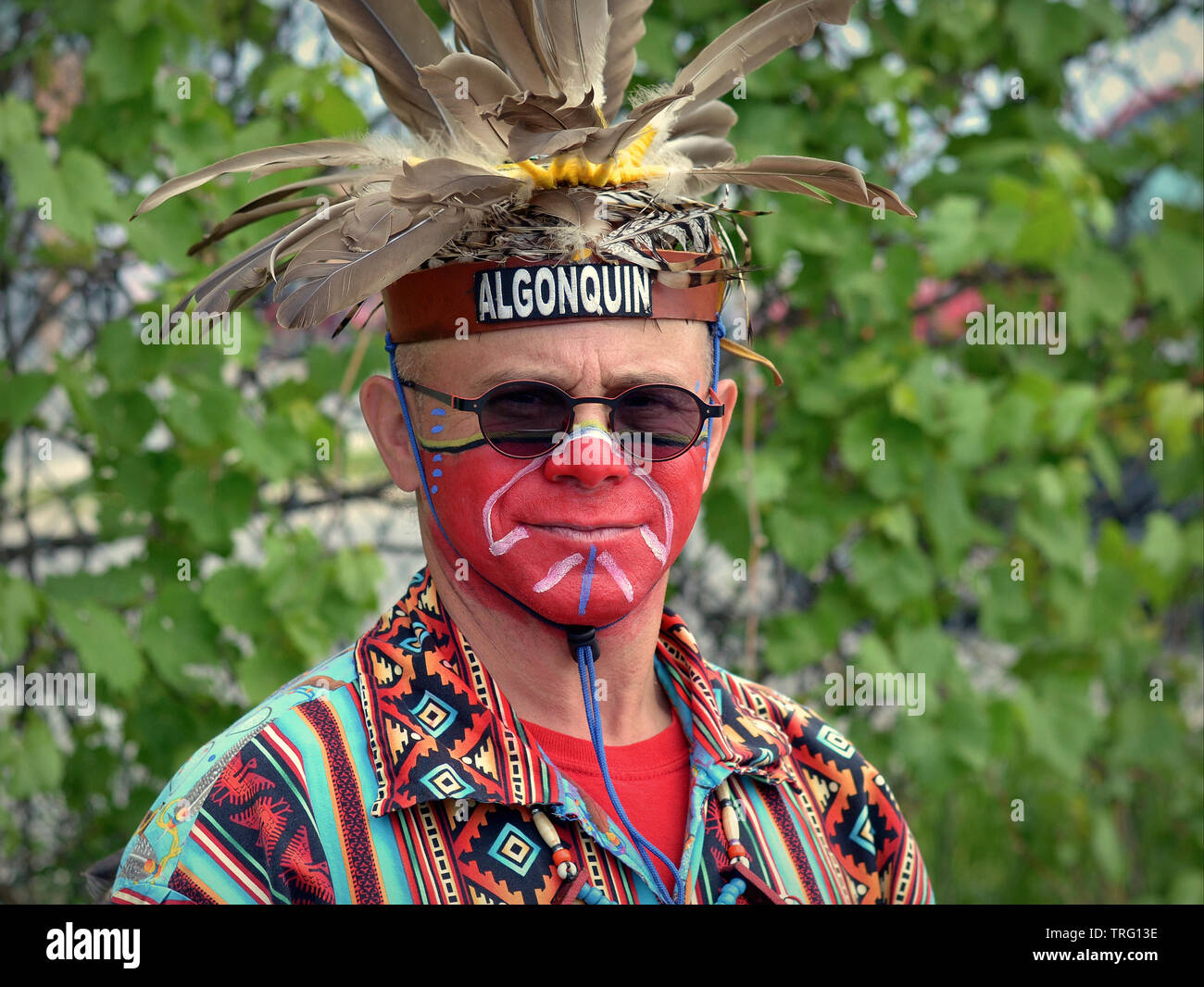 Kanadische Algonquin/Iroquois First Nations Mann mit bemaltem Gesicht trägt sein warbonnet und posiert für die Kamera bei einem Pow Wow. Stockfoto