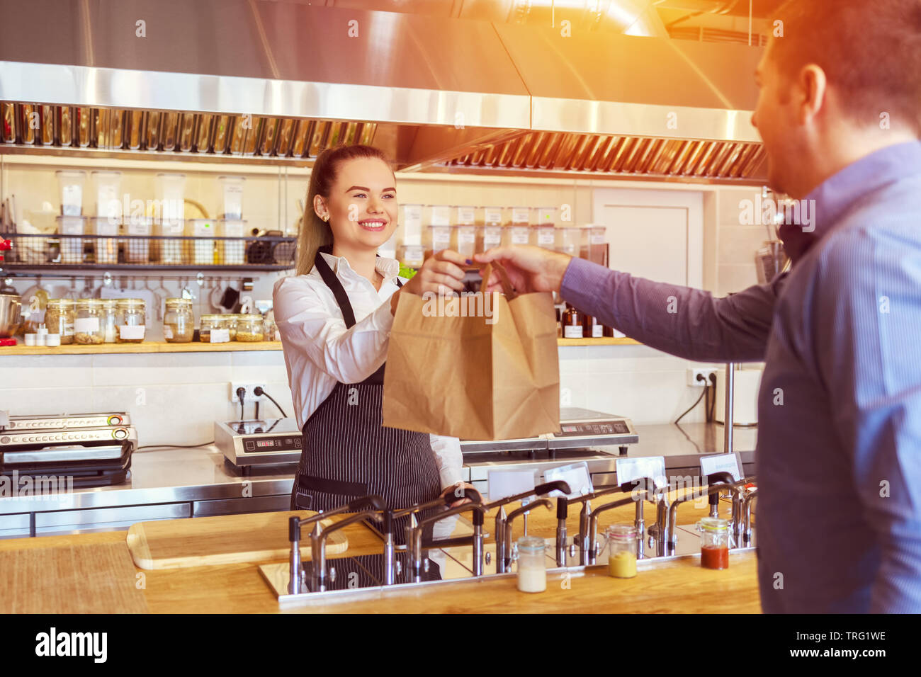 Freundliche Kellnerin von Small Business Restaurant tragen Schürze Kunden an der Theke im Restaurant in Recyclingpapier Beutel dienen Stockfoto