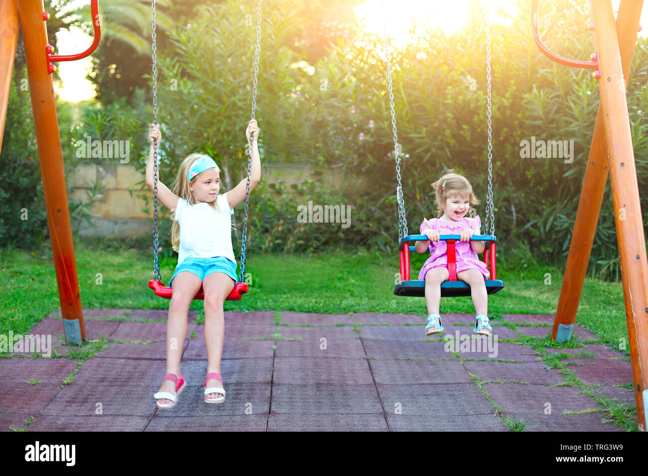 Spielende Kinder auf dem Spielplatz im Park. Zwei kleine Schwestern auf der Schaukel Stockfoto