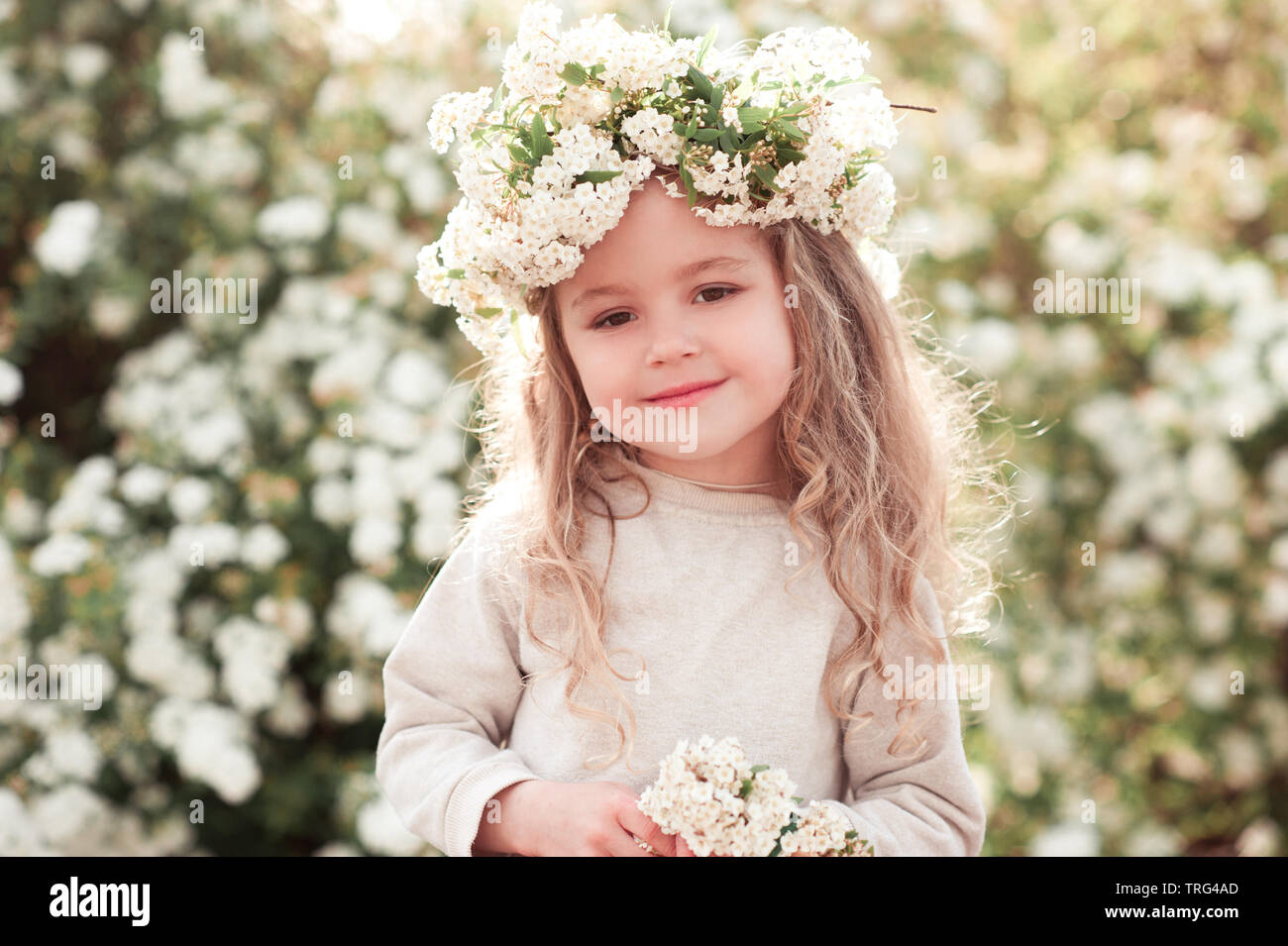 Lächelnd kind Mädchen 3-4 Jahre alt über floral background posieren. Tragen Blumenkranz im Freien. Mit Blick auf die Kamera. Kindheit. Stockfoto