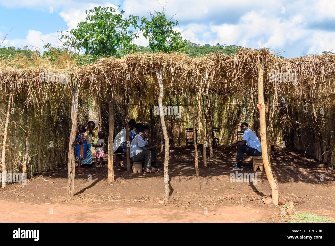 Malawische Männer sitzen auf Holzbänken unter einem Gras Tierheim aus der Sonne zu sprechen Stockfoto