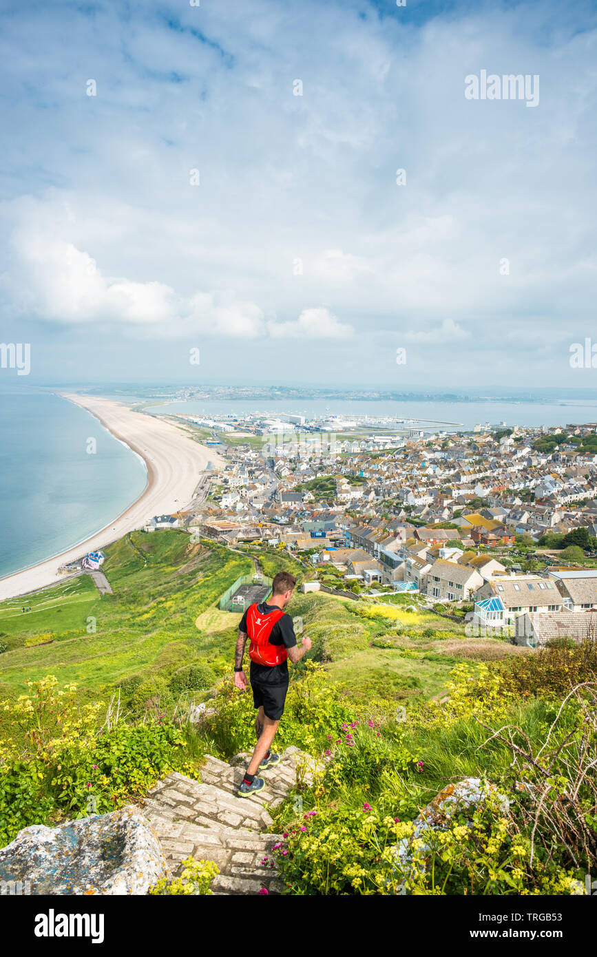 Jogger läuft steilen Weg von Portland Höhen auf der Isle of Portland in Richtung Chesil Beach und der viilage der Fortuneswell, Dorset, England, UK. Stockfoto