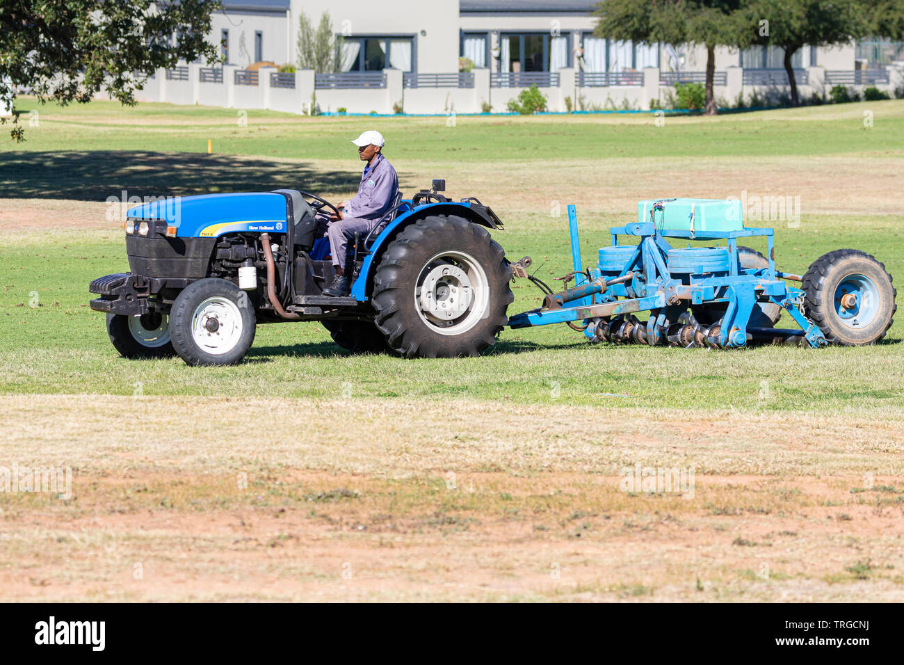 Arbeitnehmer Anritzen der Fahrrinne rasen auf einem Golfkurs mit Traktor und vertikutierer vor der Aussaat neue Gras Stockfoto