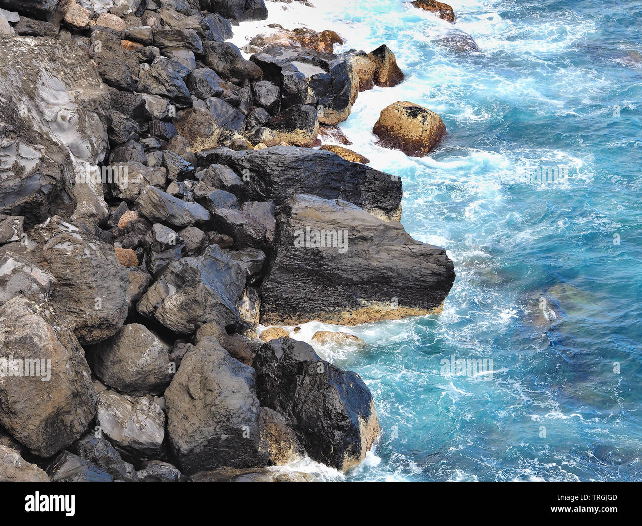 Natürliche Steine von schwarz glänzende Lava, die wilde Küste im Norden von Teneriffa, davor ein blau-grüner Atlantic, alle in Nahaufnahme Stockfoto