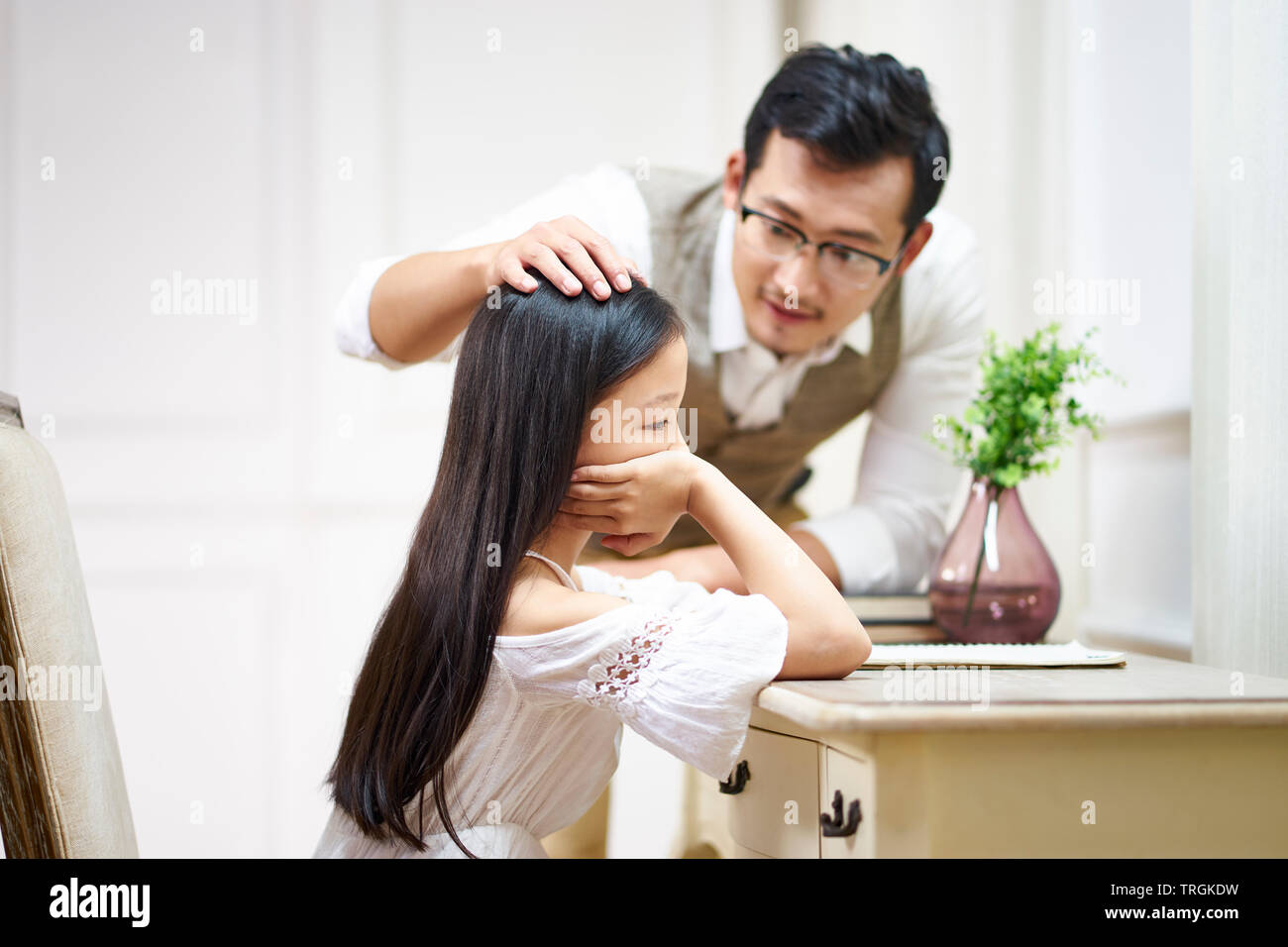 Traurigen kleinen asiatischen Mädchen sitzen am Schreibtisch in Ihrem Zimmer und Komfort von fürsorglichen Vaters Stockfoto