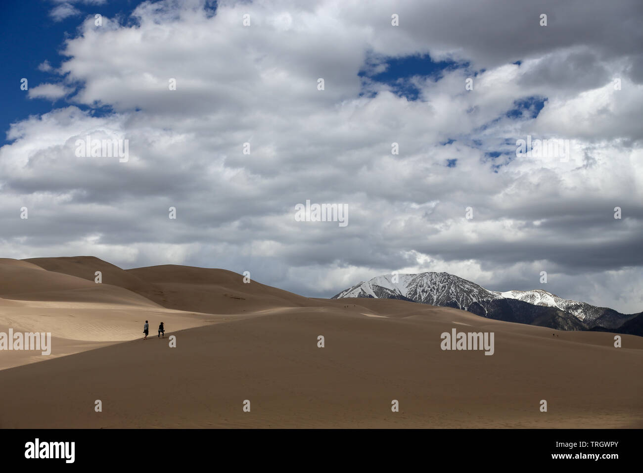 Zwei Menschen, die über die Wüste Sand Dünen mit Schnee bedeckte Bergkette in Colorado Great Sand Dunes National Park Stockfoto