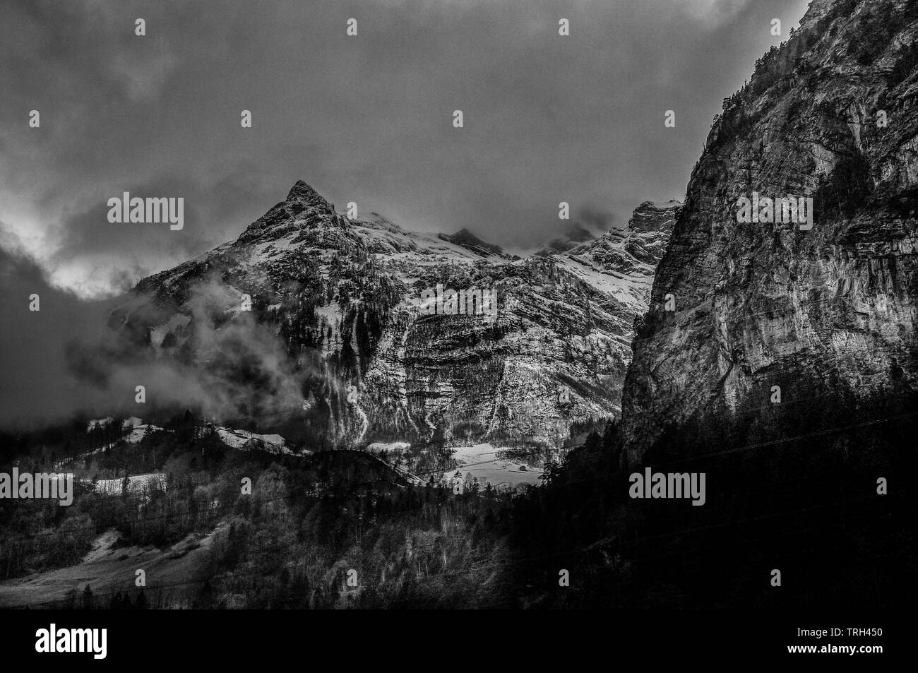 Ein Sturm macht sich über die schneebedeckten Alpen in Bellinzona, Schweiz, wo die schwarzen Wolken sind Engulfing die Alpen verlassen unter einer verschneiten Tal. Stockfoto