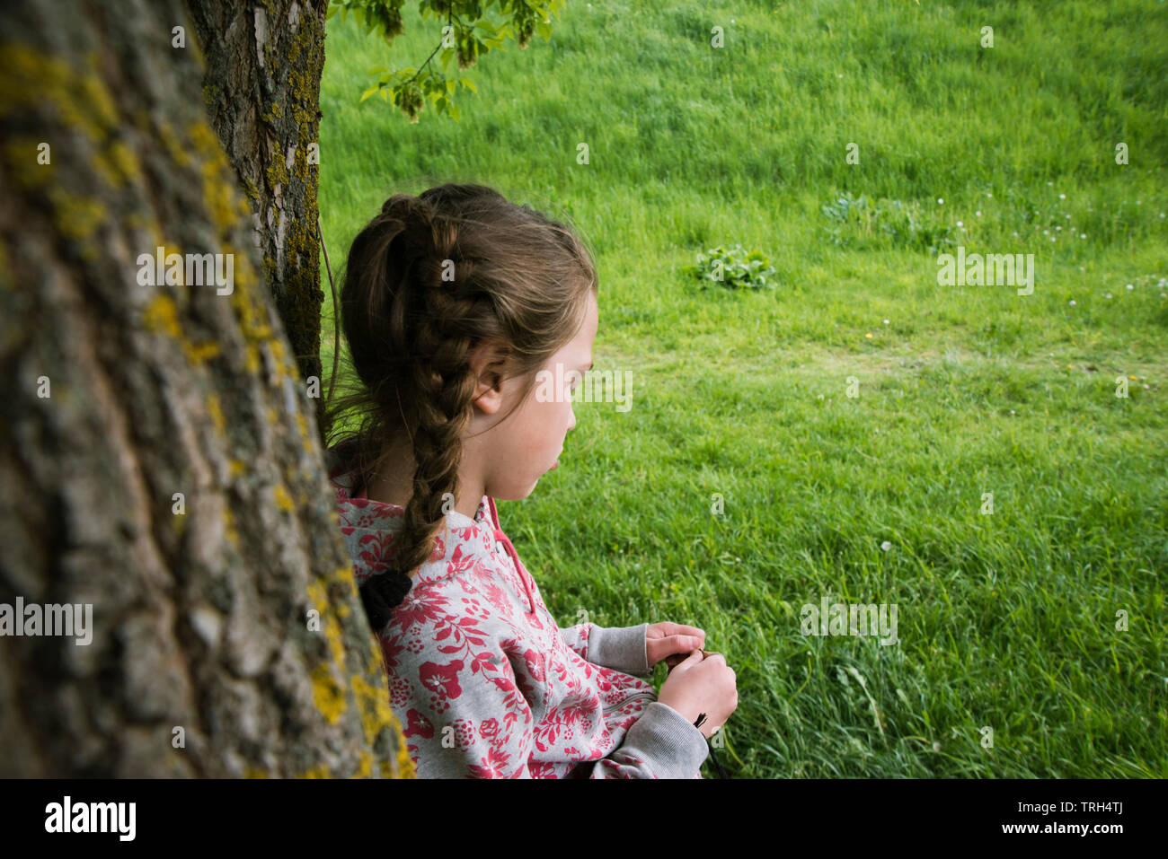 Mädchen lehnte sich auf Baumstamm im Freien in finsteren Stimmung Stockfoto