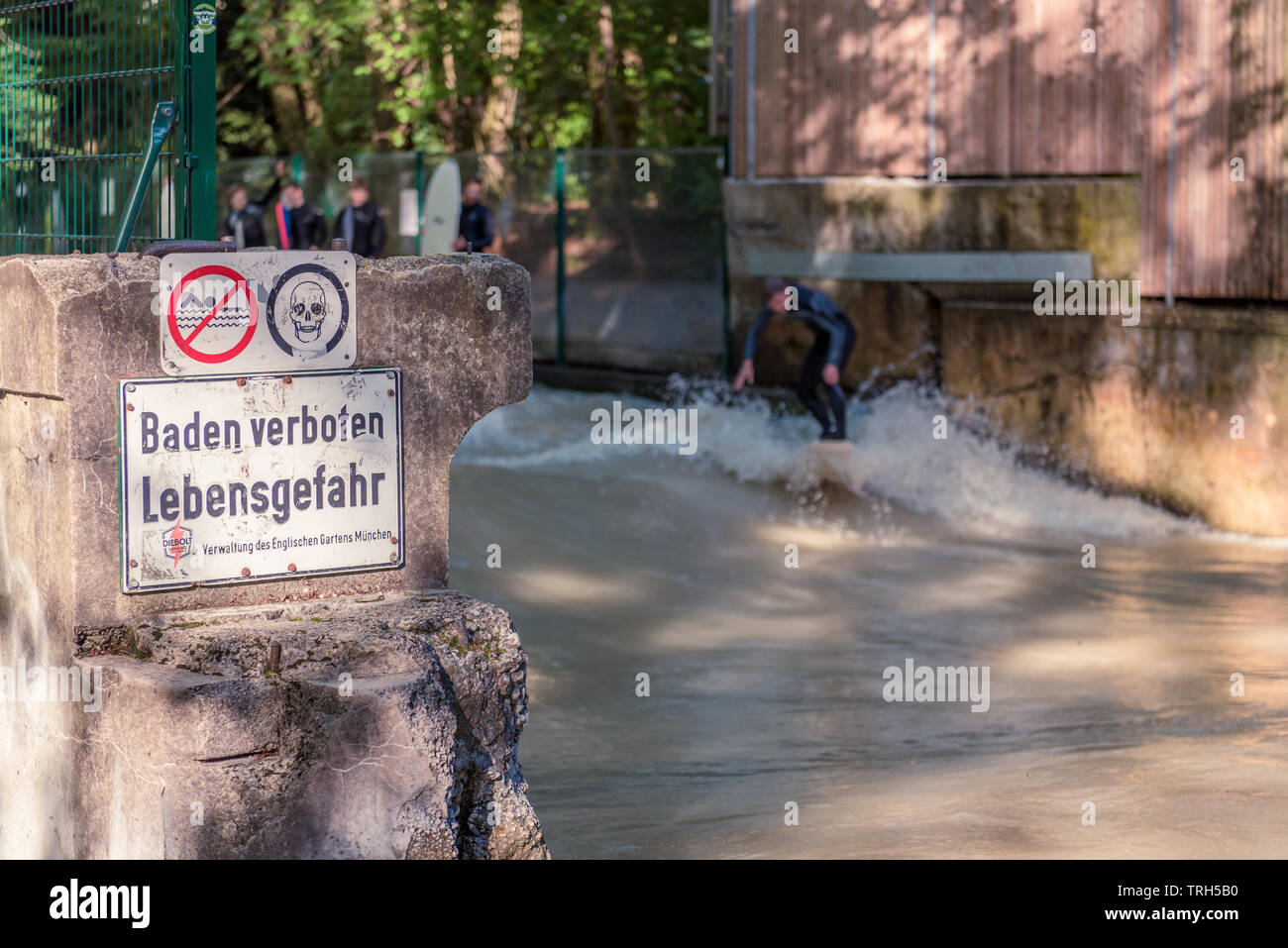 Männliche Surfer auf der Isar, der durch den Englischen Garten in München läuft, Deutschland mit Warnzeichen. Stockfoto
