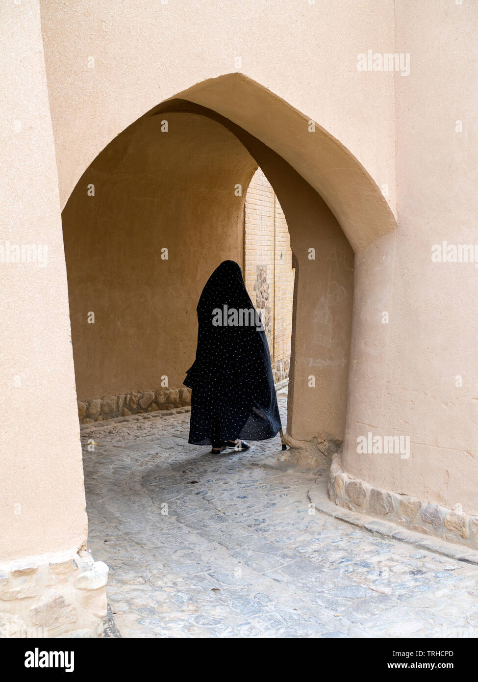 Eine Frau geht durch einen Torbogen in der Altstadt von Aqda, Iran Die Stadt wird derzeit für Tourismus restauriert. Stockfoto